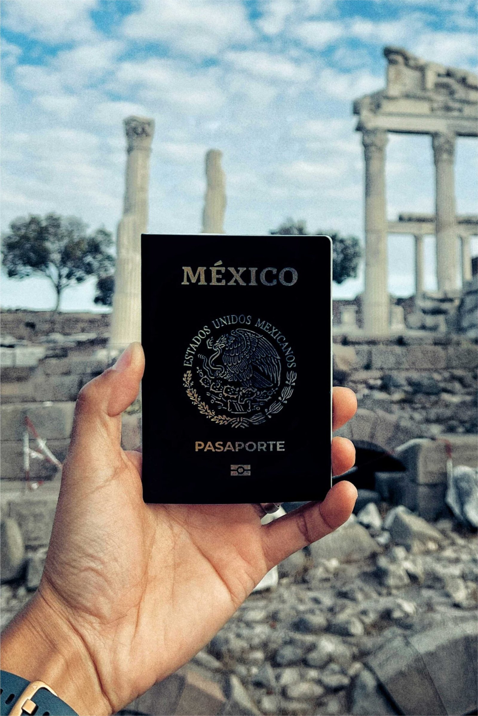 Mano sosteniendo el pasaporte mexicano con ruinas griegas de fondo